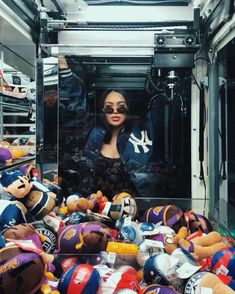 a woman standing in front of a pile of stuffed animals and baseball caps on display