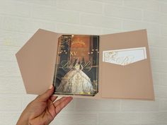 a hand holding an open book with the cover opened to reveal a wedding dress on it