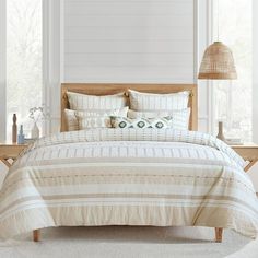 a bed with white sheets and pillows in a room next to a lamp on a table