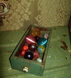 an old wooden box filled with marbles on top of a green table next to a lace covered wall