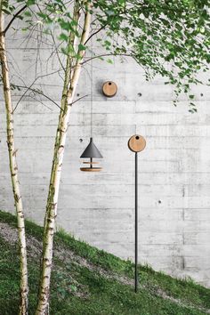 three lamps hanging from the side of a white wall next to a tree with green leaves