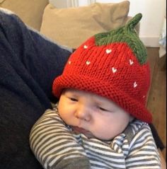 a baby wearing a knitted strawberry hat on top of it's mother's lap