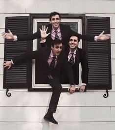 three men in suits and ties standing on a window sill with their hands up