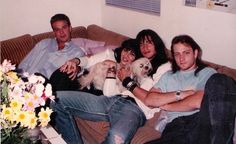 a group of people sitting on a couch with a dog in their lap and one person holding a small white dog