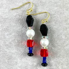 Christmas Toy Soldier Bead Earrings. Adorable toy solider dangle earrings made up of glass and acrylic beads varying in size and shape. Each earring has a gold-plated ear wire, gold tone headpin, glass & acrylic beads, faux pearl bead, and rondelle rhinestone beads. Clear plastic earring backs included with earring purchase. It is recommended that you store the earrings without the earring backs on as it may oxidize the metal finish.  Length: 20mm (Including Earwire) Width: 7.8mm Square Red Bead Beaded Nutcracker Earrings, Diy Earrings Dangle, Christmas Toy Soldiers, Christmas Jewelry Diy, Soldier Boy, Plastic Earrings, Christmas 2017, Rhinestone Bead, Toy Soldiers