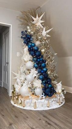 a decorated christmas tree with blue and white ornaments in a living room next to a doorway