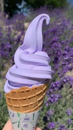 a hand holding an ice cream cone with lavender flowers in the background