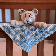 a crocheted teddy bear sitting on top of a wooden chair with a blue and white blanket