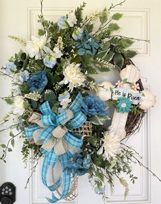 a wreath on the front door decorated with blue and white flowers, greenery and a ribbon