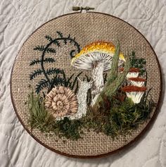 a close up of a cross stitch on a table cloth with mushrooms and plants in it