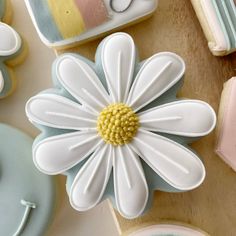 decorated cookies with white and yellow flowers sitting on top of a wooden table next to cookie cutters