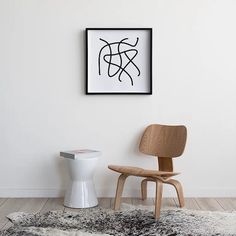 a white toilet sitting next to a wooden chair in a room with a black and white painting on the wall