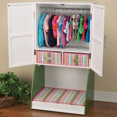 a white cabinet with drawers and clothes hanging on the door, next to a potted plant