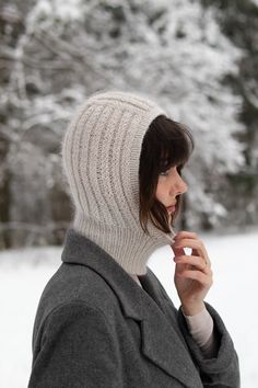 a woman wearing a knitted hat and coat in the snow with trees behind her