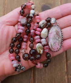 Indulge in the enchanting blend of pink and brown hues with this exquisite necklace, featuring a harmonious mix of strawberry quartz, smoky quartz, rhodochrosite, and Czech crystals. Each stone is carefully selected to create a captivating contrast that is both striking and elegant. Handcrafted with meticulous attention to detail, this necklace showcases varying stone sizes that add depth and intrigue to the design. Measuring 24 inches in length and secured with a lobster claw clasp, it offers both style and versatility. At its focal point hangs a mesmerizing rhodochrosite pendant set in a crown artisan setting, measuring 2 3/8 inches long. Rhodochrosite is known for its properties of promoting love, compassion, and emotional healing, making this necklace not only a stunning accessory but Bohemian Pink Agate Necklace, Pink Tourmaline Bohemian Jewelry, Pink Natural Stones Beaded Necklace For Healing, Handmade Pink Tourmaline Necklaces, Handmade Pink Tourmaline Necklace, Necklace With Pendant, Pink And Brown, Czech Crystal, Strawberry Quartz