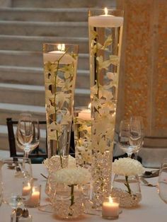 a table with candles and vases filled with white flowers next to some glass wine glasses