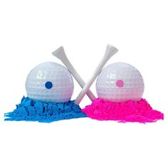 two white golf balls with pink and blue shavings on the ground next to each other