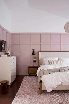 a bed room with a neatly made bed next to a pink wall and a white dresser