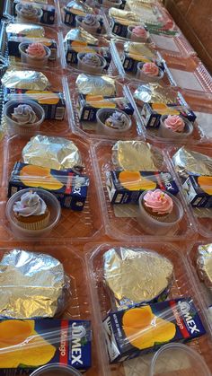 some cupcakes are sitting in plastic containers on a table with foil wrappers