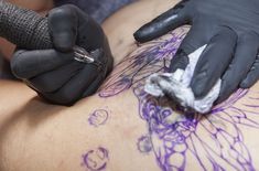 a person with black gloves and tattoos on their back getting ink applied to the chest