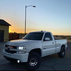 a white pickup truck parked in a parking lot at sunset with the sun setting behind it