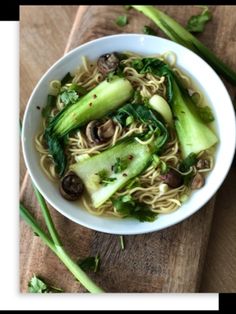 a white bowl filled with noodles and vegetables on top of a wooden cutting board next to green onions