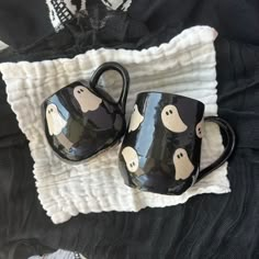 two black mugs with ghost faces on them sitting on a white towel next to each other