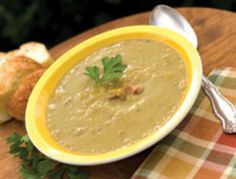 a yellow bowl filled with soup on top of a table next to bread and spoon