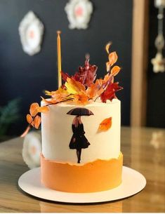 a white cake with orange and yellow leaves on it's side, topped with an umbrella