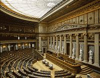 the interior of a large building with rows of seats in front of an ornate ceiling