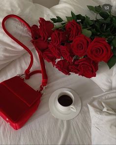 a red purse sitting on top of a white bed next to a cup of coffee