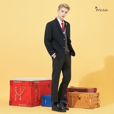 a young man in a suit and tie standing next to suitcases on a yellow background