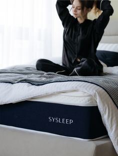 a woman sitting on top of a bed next to a mattress with the word syslep written on it