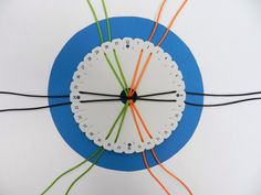 a white clock with orange and green wires connected to it on a blue circular surface