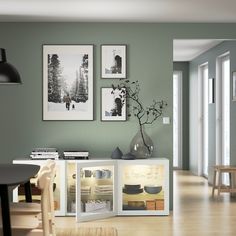 a dining room with green walls and pictures on the wall, including a vase filled with flowers