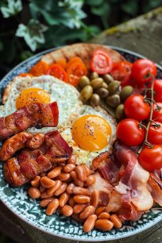 a plate with eggs, bacon, tomatoes and beans on it