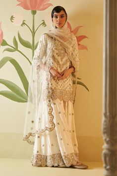 Ivory kurta with floral, gotta patti, mirror work, zari embroidery. Paired with embroidered sharara and embroidered dupatta.
Components: 3
Pattern: Embroidered
Type Of Work: Floral
Neckline: Tier drop neck
Sleeve Type: Three quarter
Fabric: Silk, Lining: Crepe
Color: Ivory
Other Details: 
Attached lining
Side slits
Back tie-up
Scallop border dupatta
Note: All the jewellery worn by the model is for styling purpose only
Occasion: Wedding - Aza Fashions Off White Sharara With Resham Embroidery For Reception, Off White Resham Embroidered Sharara For Reception, Off White Resham Embroidery Sharara For Reception, Wedding Palazzo Set With Intricate Embroidery In Cream, Cream Palazzo Set With Resham Embroidery For Wedding, Elegant Off White Sharara With Intricate Embroidery, Beige Resham Embroidery Palazzo Set For Wedding, Elegant Off White Georgette Sharara, Elegant Off-white Georgette Sharara