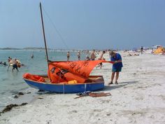 a small boat on the beach with people in the water and one person standing next to it