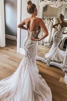 a woman in a wedding dress looking at herself in the mirror with her back to the camera