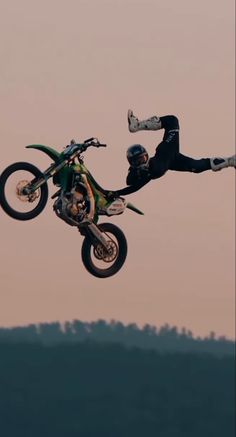 a man flying through the air while riding on top of a dirt bike in front of a sunset sky