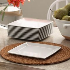 a stack of white plates sitting on top of a table next to a bowl of fruit