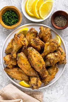 a white plate topped with chicken wings next to bowls of lemons and seasoning