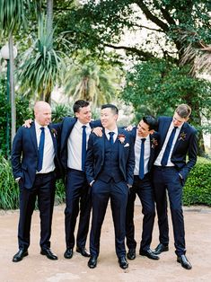 a group of men in suits standing next to each other on a dirt ground with trees and bushes behind them