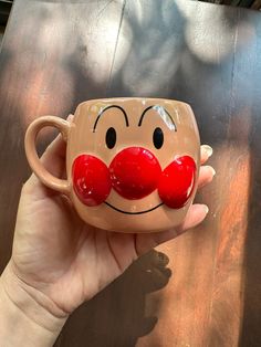 a hand holding a coffee mug with a red nose and mustache painted on the side