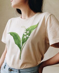 Celebrate May Birth Flower with our Lily of the Valley t-shirt. This original watercolor print that you will not find anywhere else will make a perfect gift for someone who celebrates a birthday in May. Printed on a cotton t-shirt, made from durable lightweight cotton. Unisex fit - boxy and long. How it's made: * All prints are original watercolor designs hand-painted by a botanical artist. * Ethically made 100% cotton t-shirts that are made to last. * T-shirts are printed and shipped by my prin White Watercolor Print T-shirt For Spring, Spring Gift White T-shirt, Hand Painted White T-shirt For Summer, Plants Print Crew Neck T-shirt Gift, Floral Print Graphic Tee T-shirt As Gift, Plants Print Crew Neck T-shirt For Gift, Crew Neck T-shirt With Plants Print, Spring Gift T-shirt With Graphic Print, Spring Graphic Print T-shirt Gift