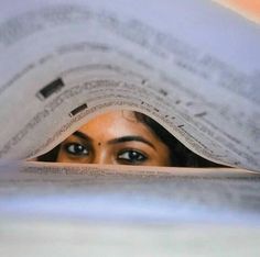 a woman peeking out from under a pile of newspapers