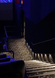 an empty auditorium with blue lighting and black carpeted steps leading up to the stage