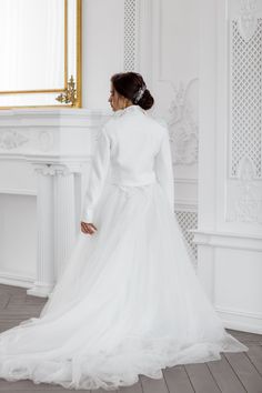 a woman in a white wedding dress standing next to a wall with a mirror on it