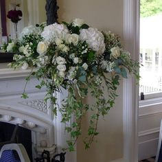 a vase with white flowers and greenery in front of a fireplace