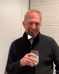 an older man holding a glass with something in it's mouth and smiling at the camera